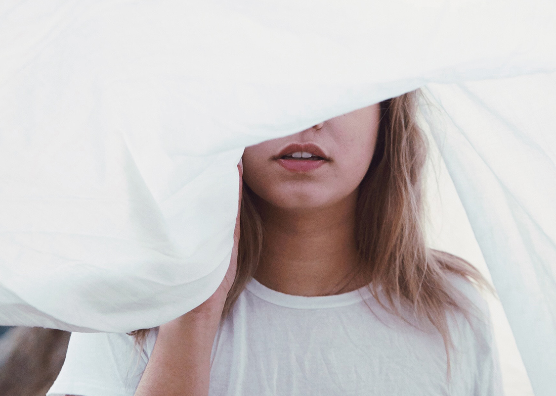 Fotografia di donna con volto in parte coperto da lenzuolo bianco