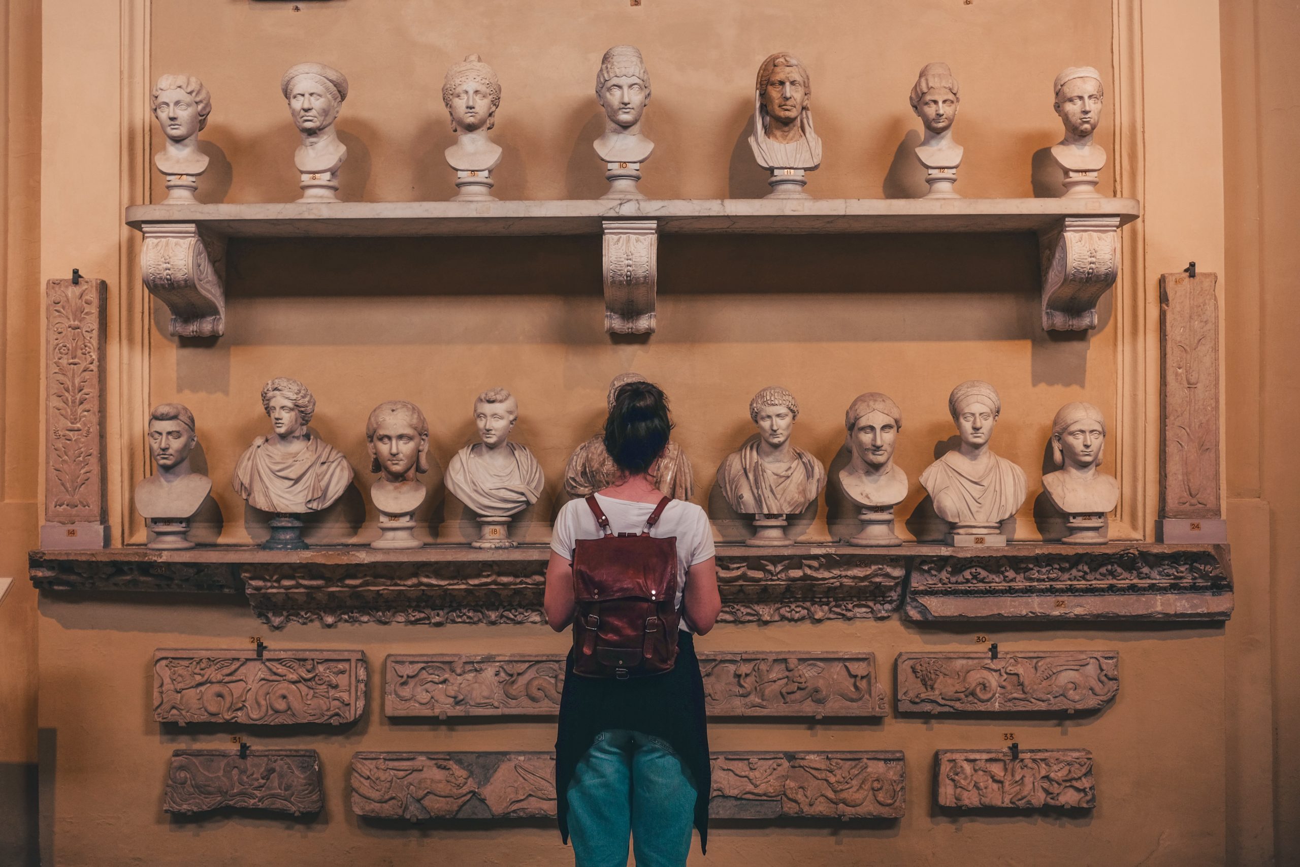 Fotografia di una ragazza di spalle di fronte a dei busti marmorei