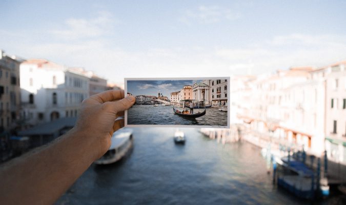 fotografia in cui una mano regge su uno sfondo di Venezia un'immagine cartacea della stesso scorcio