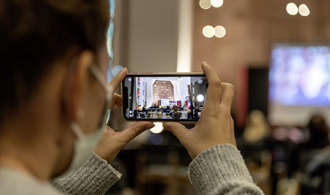 Fotografia di una persona di spalle che sta fotografando una conferenza con uno smartphone