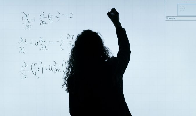 Fotografia di una donna che sta scrivendo formule matematiche alla lavagna