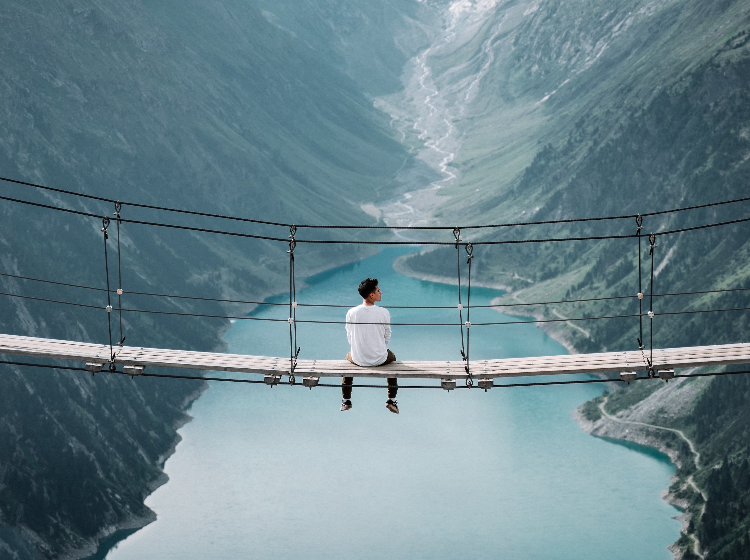 Fotografia di un uomo seduto su un ponte sospeso nel vuoto